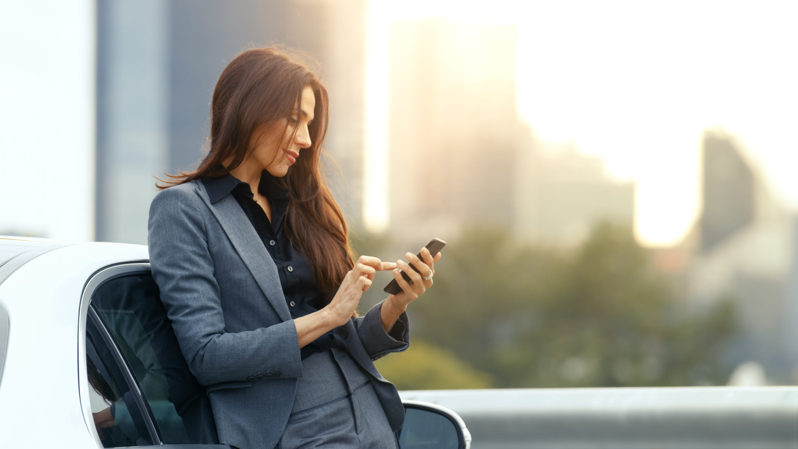donna che guarda lo smartphone appoggiata all'auto