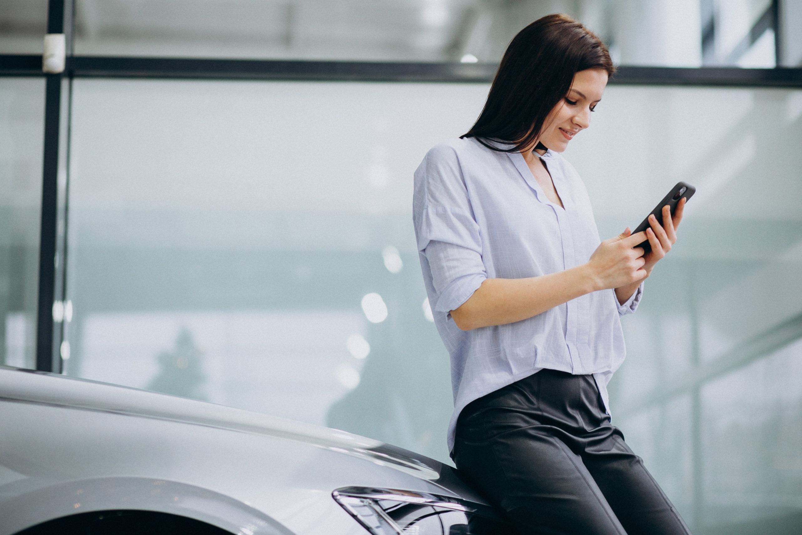 donna controlla lo smartphone appoggiata all'auto